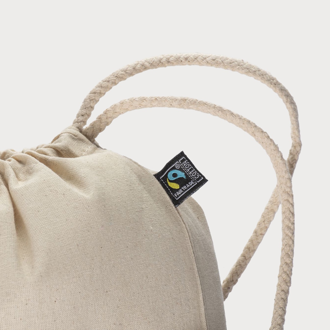 Nahaufnahme eines naturfarbenen Baumwoll-Turnbeutels, die das eingenähte Fairtrade-Cotton-Label und die gedrehte Kordel zeigt.